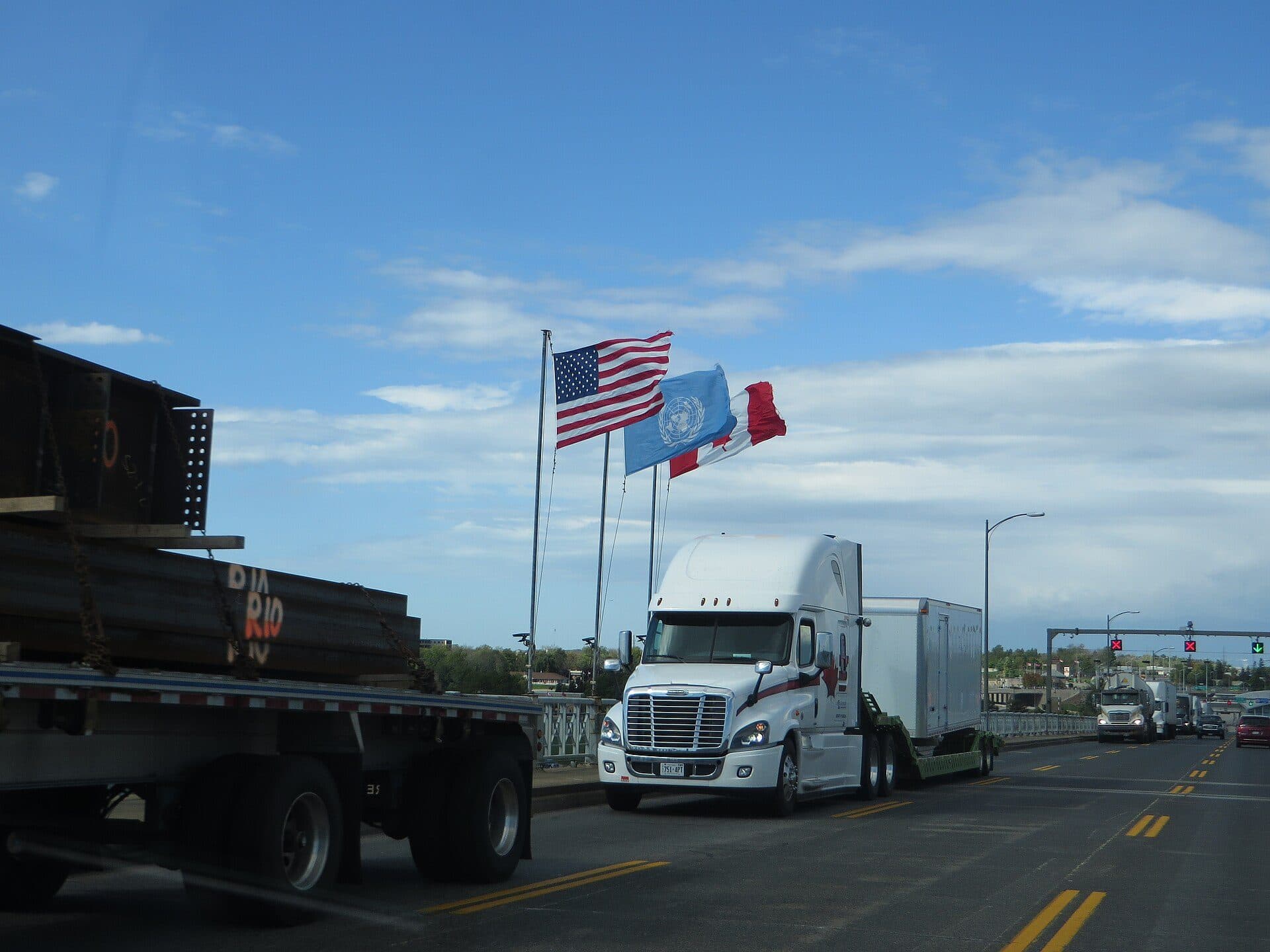 Loaded flatbed trailer at a roadside stop with a white tractor beyond