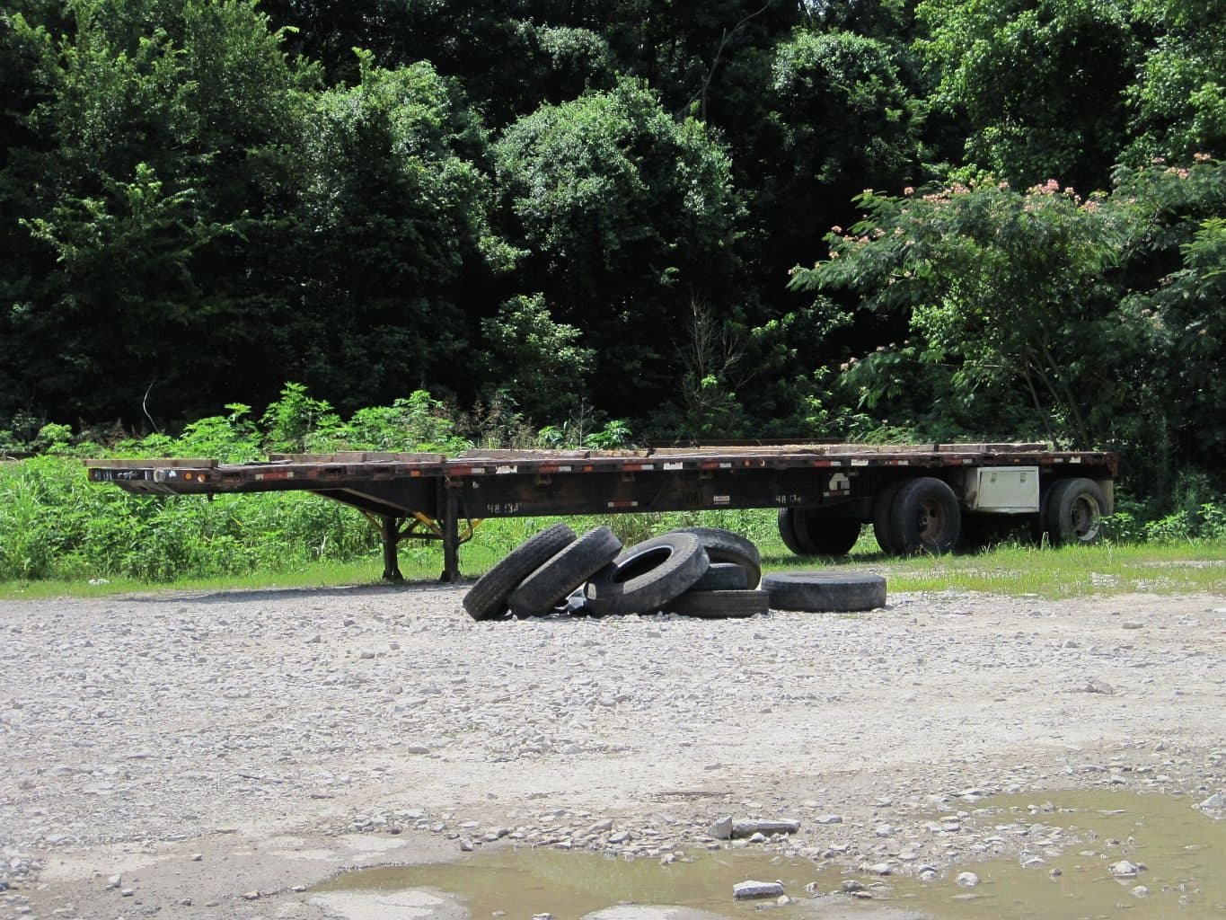 Empty flatbed trailer parked on gravel at the edge of a field