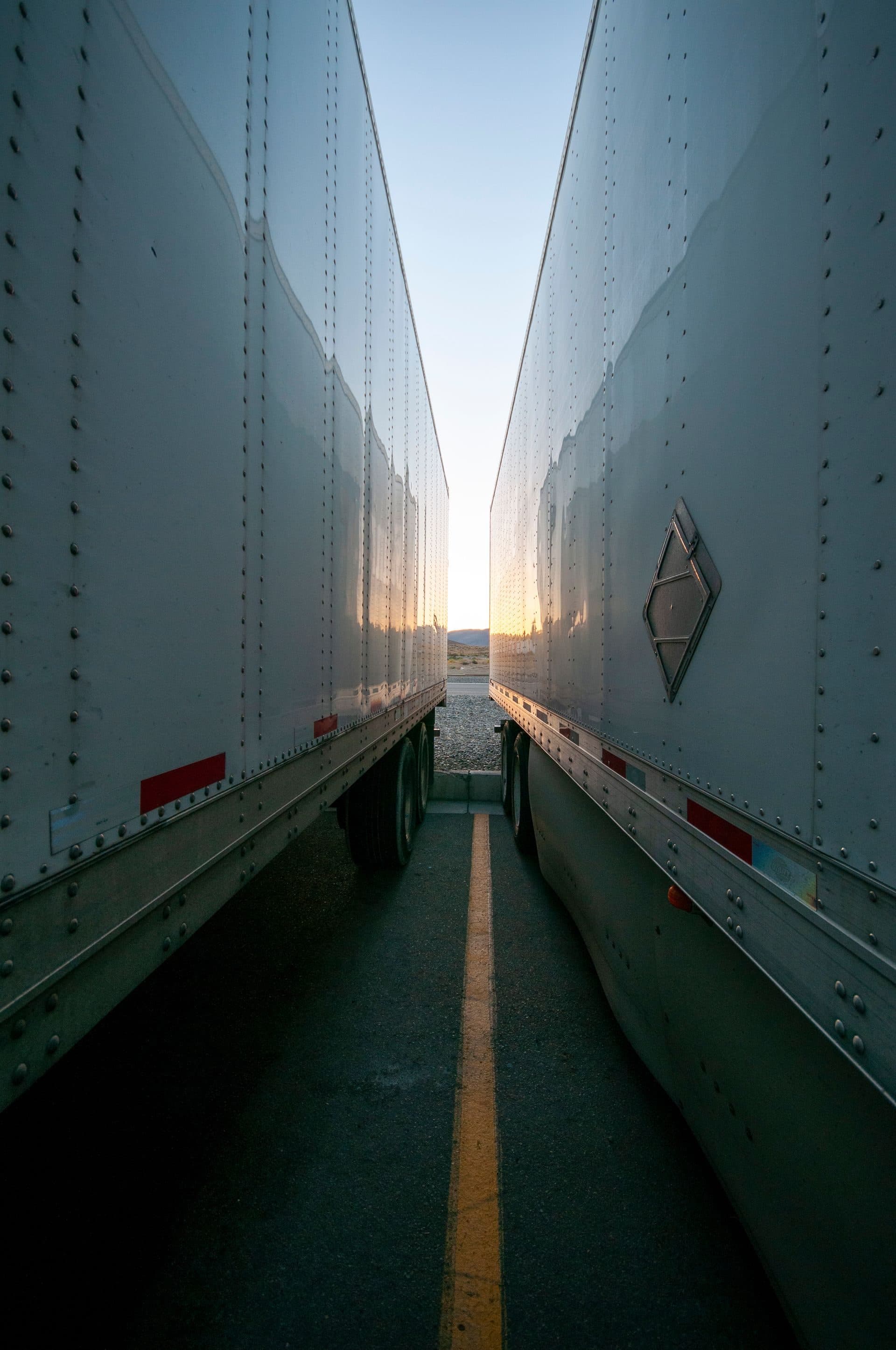 Narrow gap between two parked dry van trailers lit by a low sunset