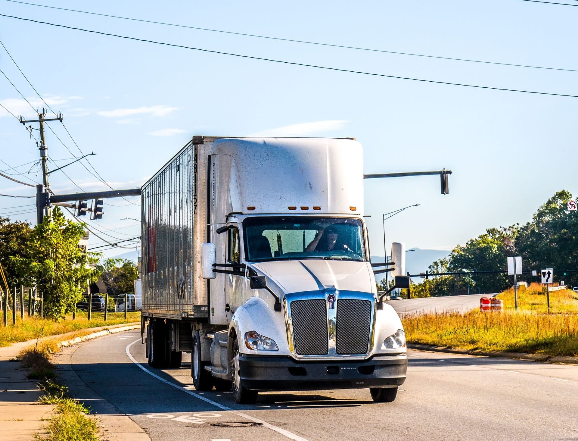 White Kenworth with a 53-foot dry van turning through a suburban intersection