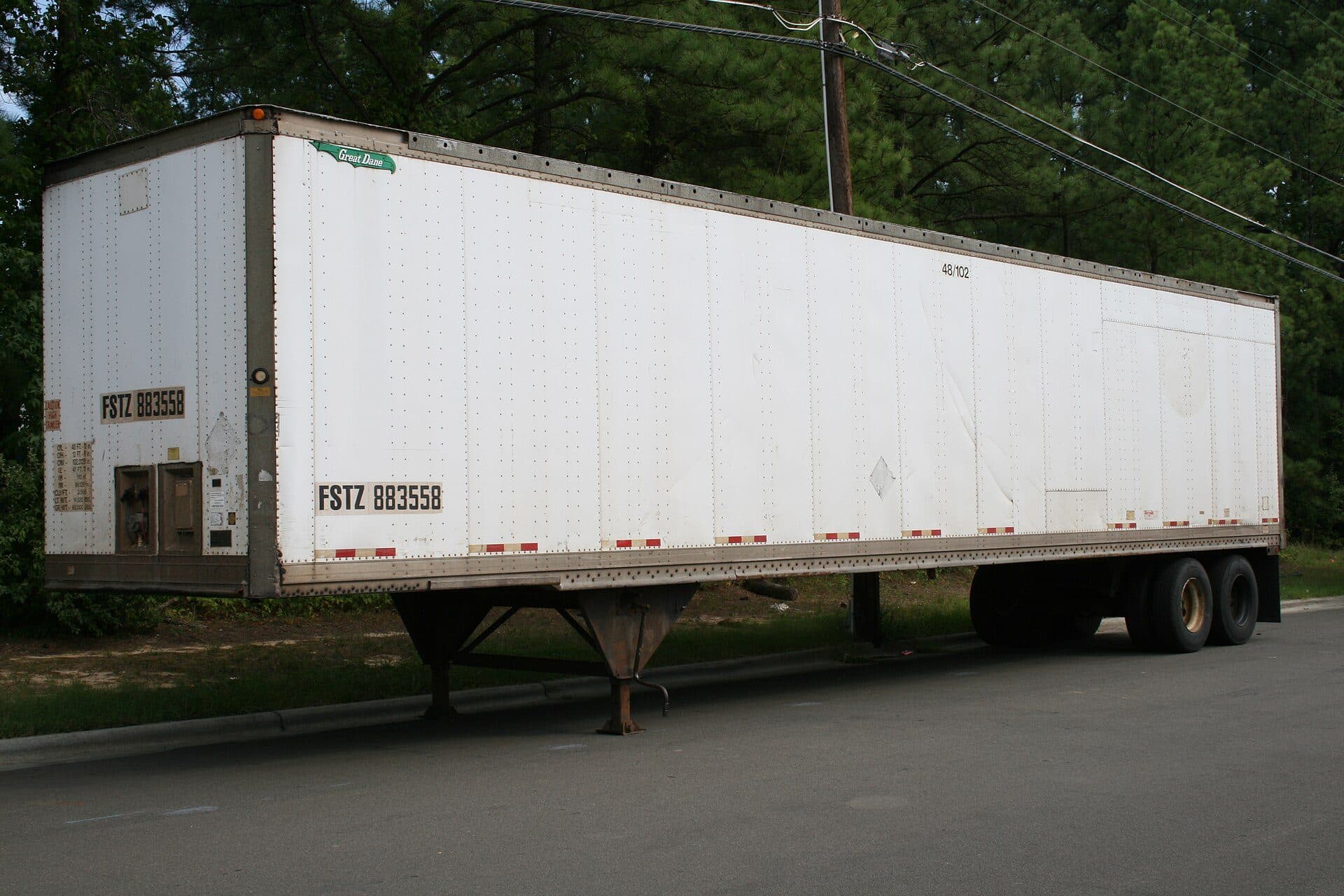 Side view of a parked white dry van semi-trailer with tandem axles