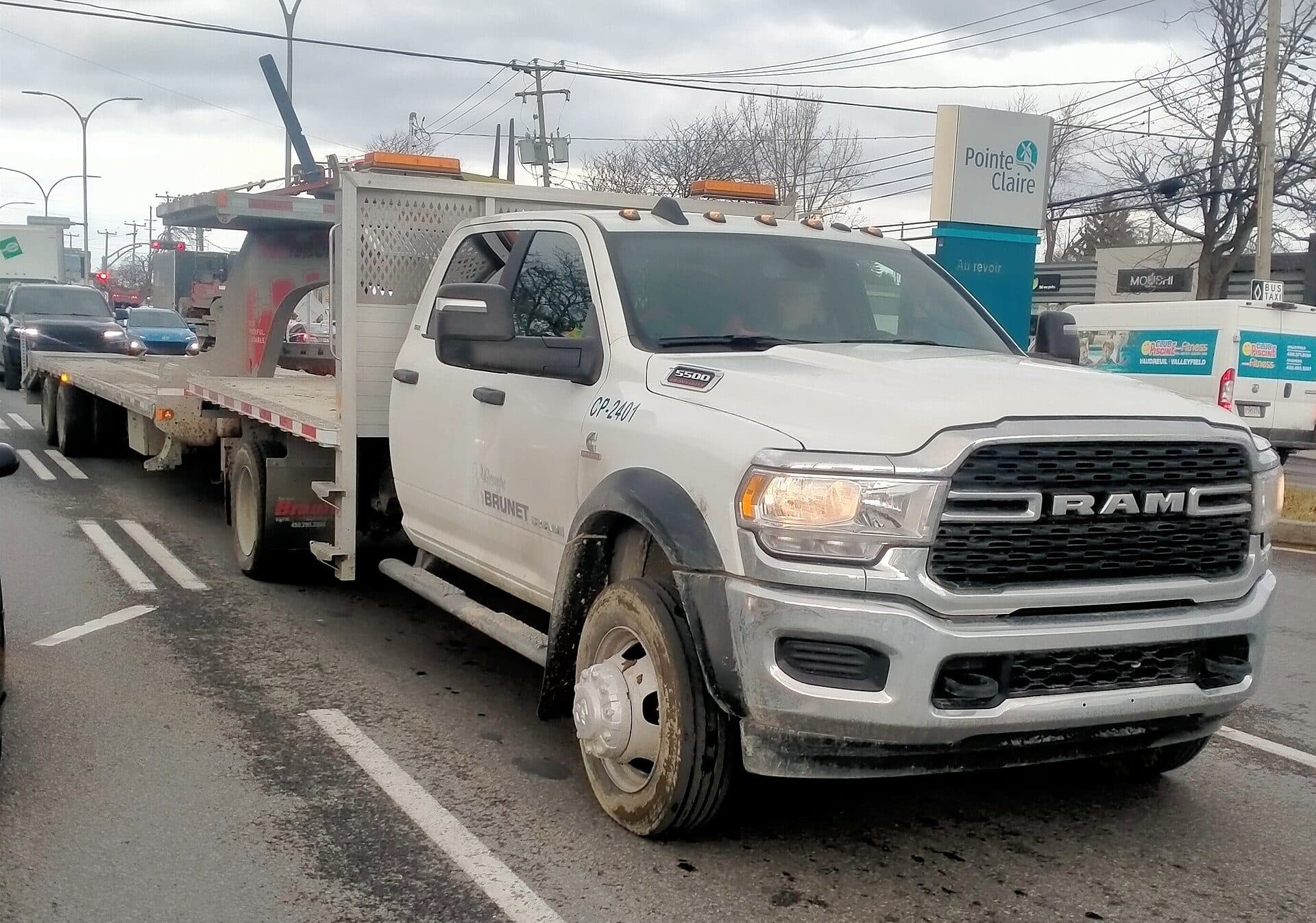 White Ram cab-chassis pulling a flatbed equipment trailer on a city street